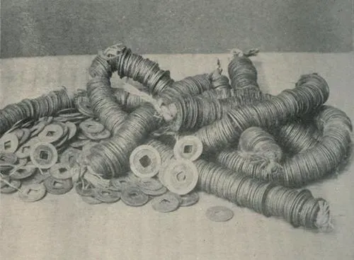 Black-and-white photo of many coins threaded into long strings, piled on a table