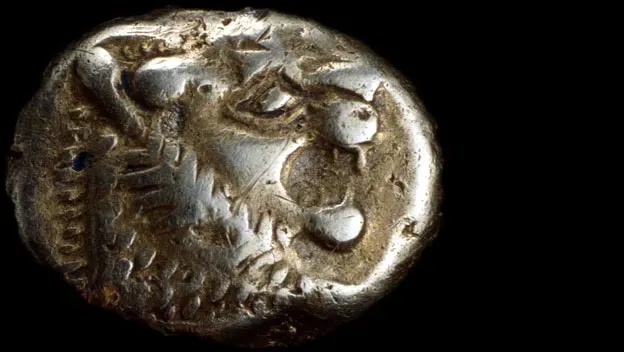 Close-up of an early stamped metal coin with a lion-like head design on a black background