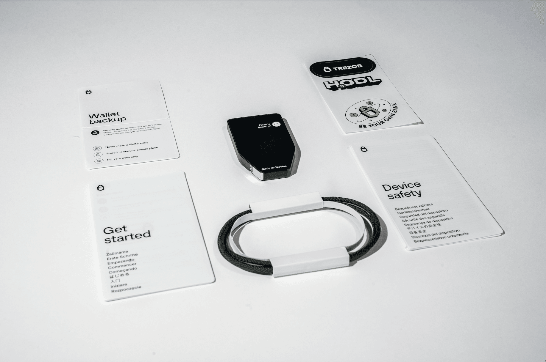 Trezor Safe 7 unboxing layout showing the device, wallet backup cards, Get started guide, device safety leaflet, USB-C cable, and Trezor stickers neatly arranged on a white surface.