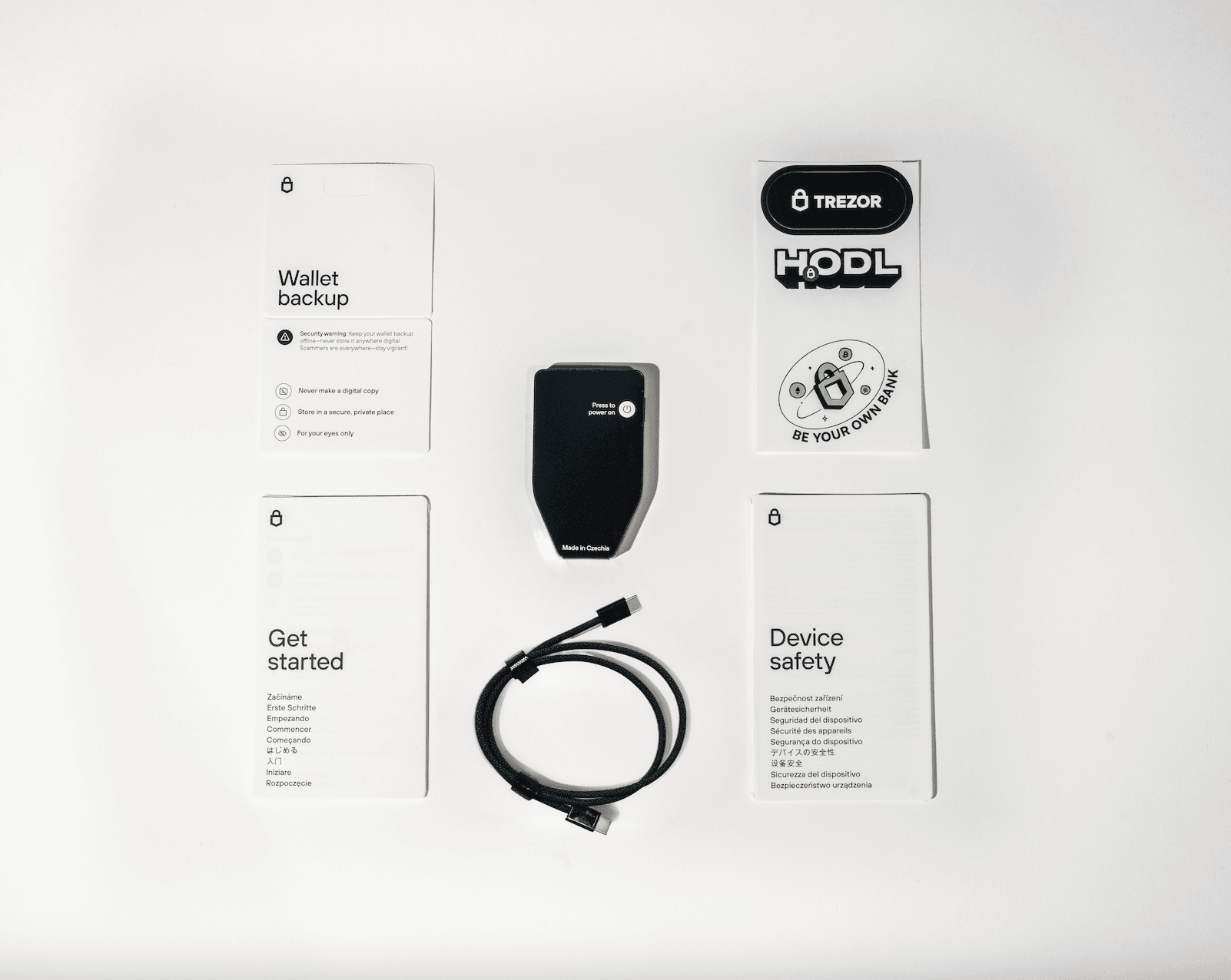 Unboxed Trezor Safe 7 hardware wallet package showing the device, USB-C cable, safety and setup guides, recovery backup cards, and branded Trezor stickers.