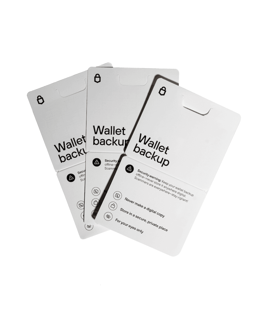 Three Trezor wallet backup cards fanned out, each labeled “Wallet backup” with printed security reminders about keeping the recovery phrase offline and private.