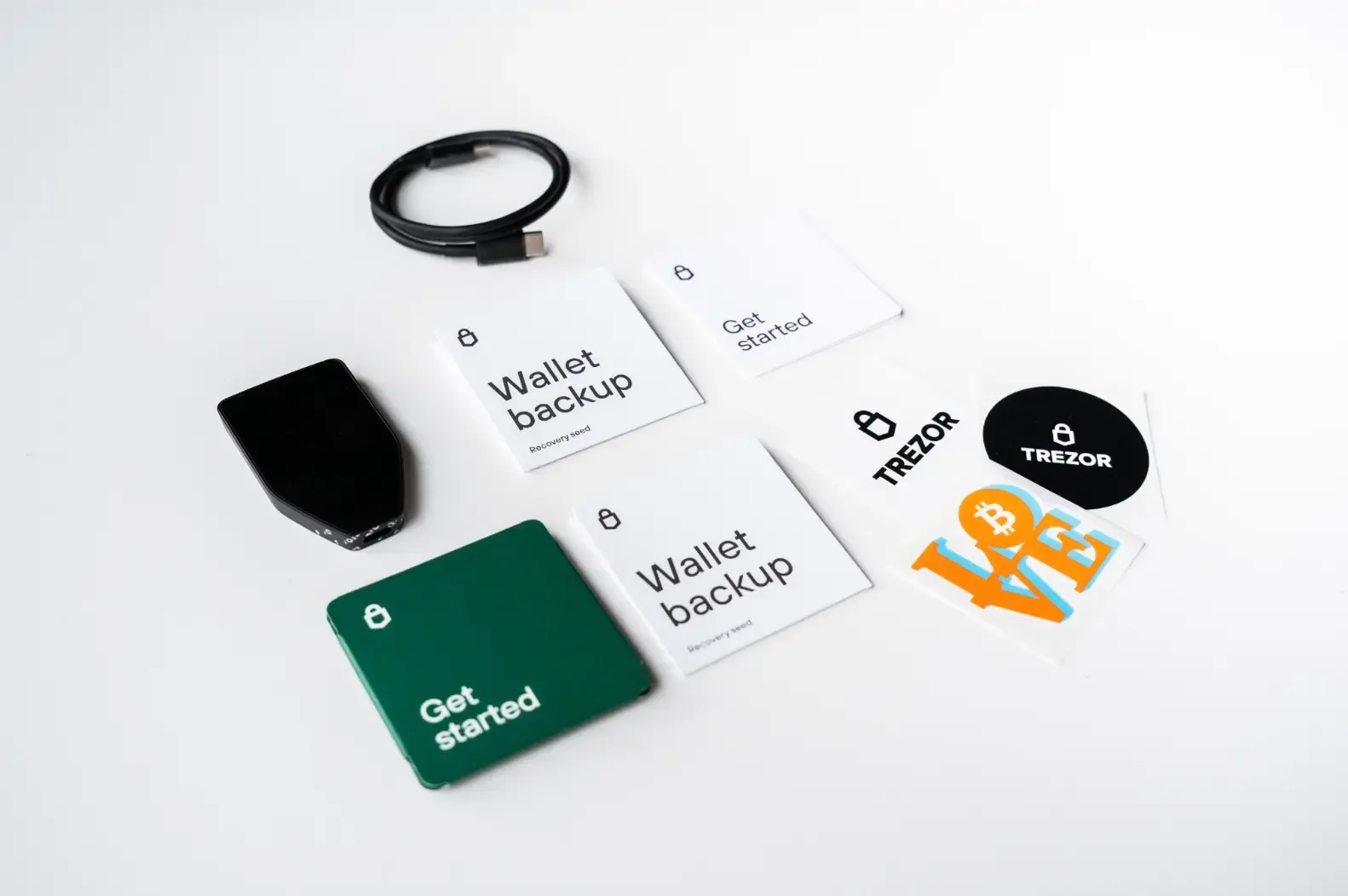 Trezor package contents laid out on a table, including device, USB cable, wallet backup cards, guide, and stickers